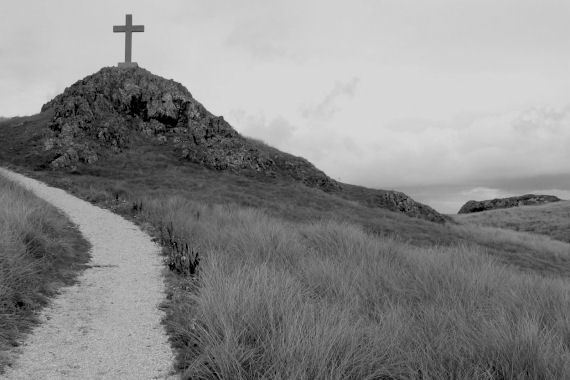 A hill with a cross on its summit and a path ascending towards it